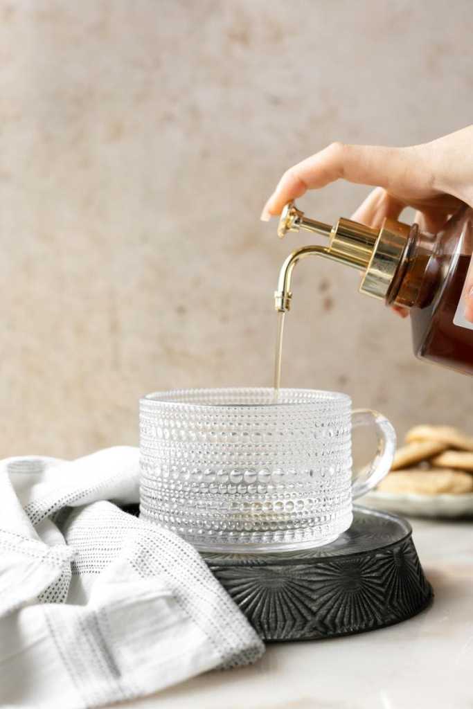 pressing down on the syrup bottle to pour the sugar cookie syrup into the cup.