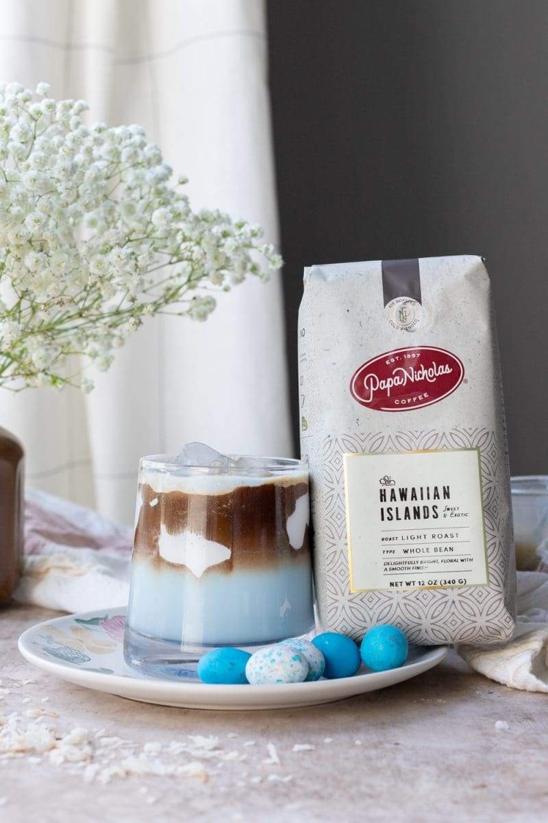 A coconut macchiato next to a bag of PapaNicholas Hawaiian Islands Espresso