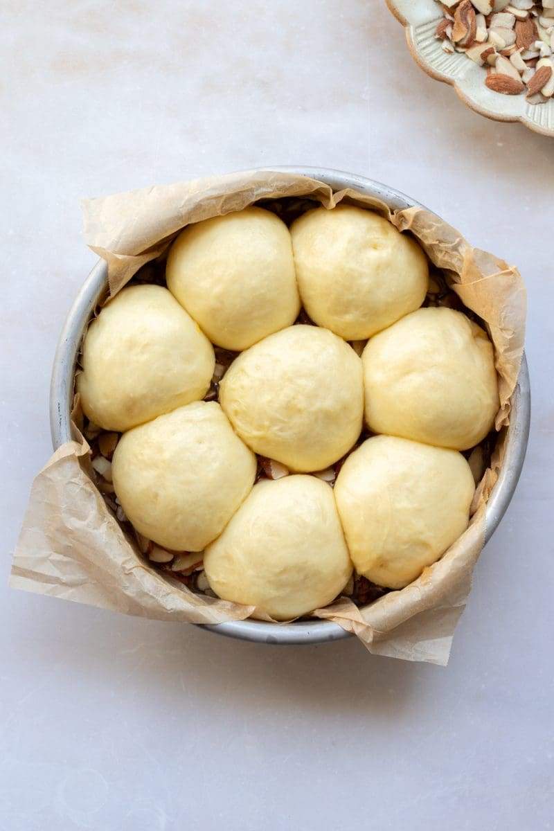 The buns in the pan, on top of the honey almond topping.