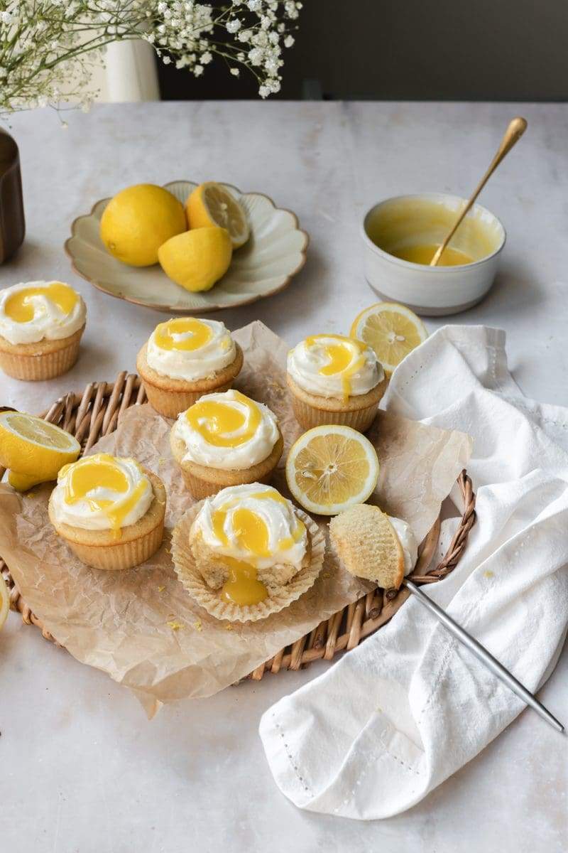 stylized image of the lemon curd cupcakes on a tray, surrounded by lemons and a bowl of lemon curd