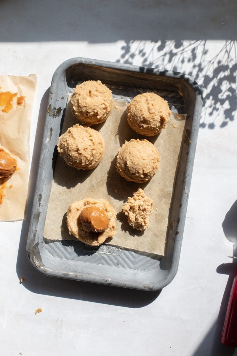 Cookie dough balls on a tray, being stuffed with a ball of frozen dulce de leche.