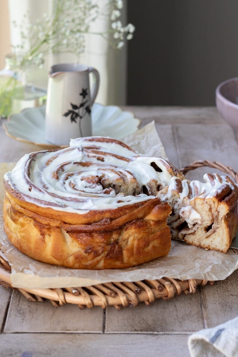 The giant cinnamon roll cake with a slice being pulled from it.
