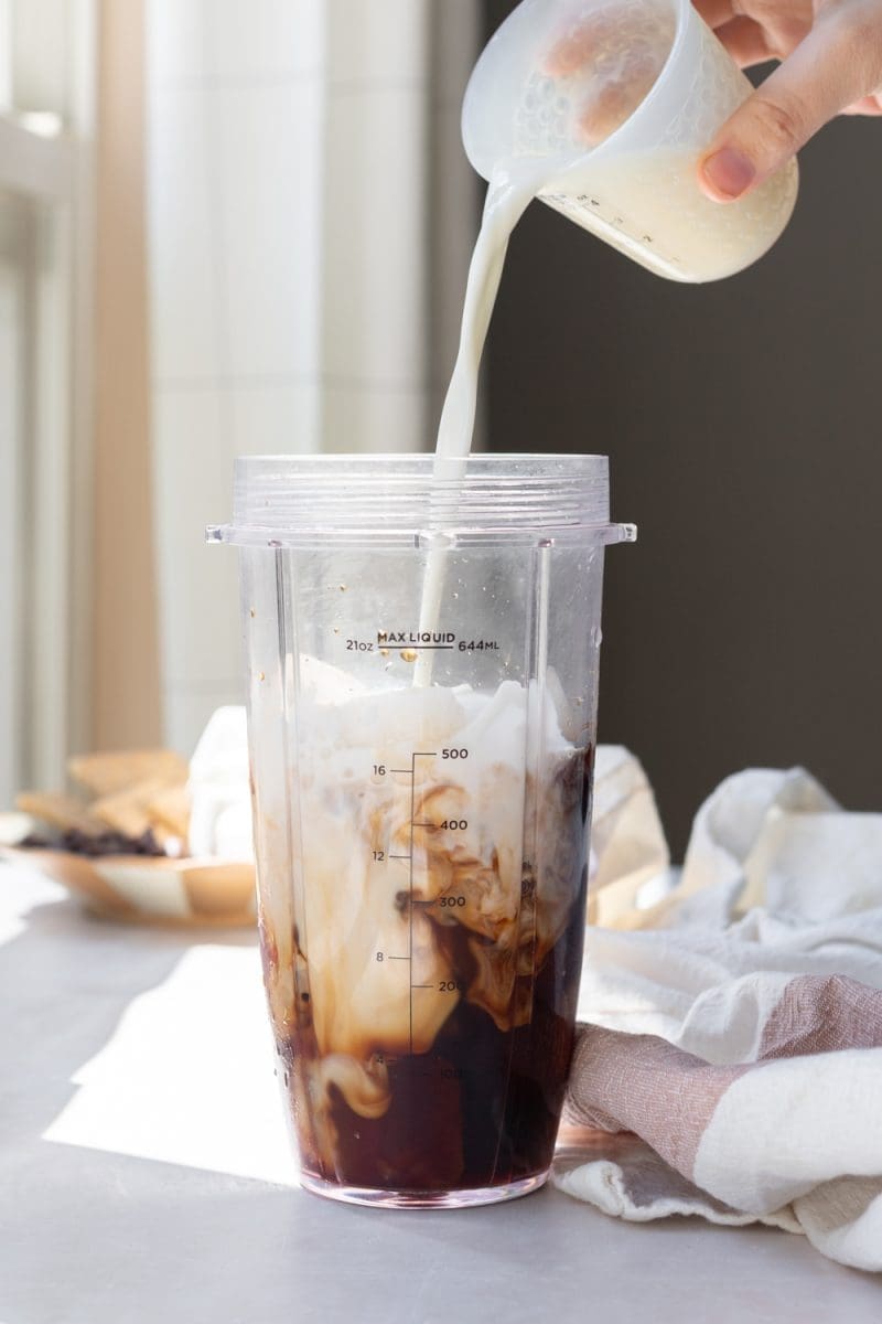 Pouring milk into the blender along with the ice and coffee.
