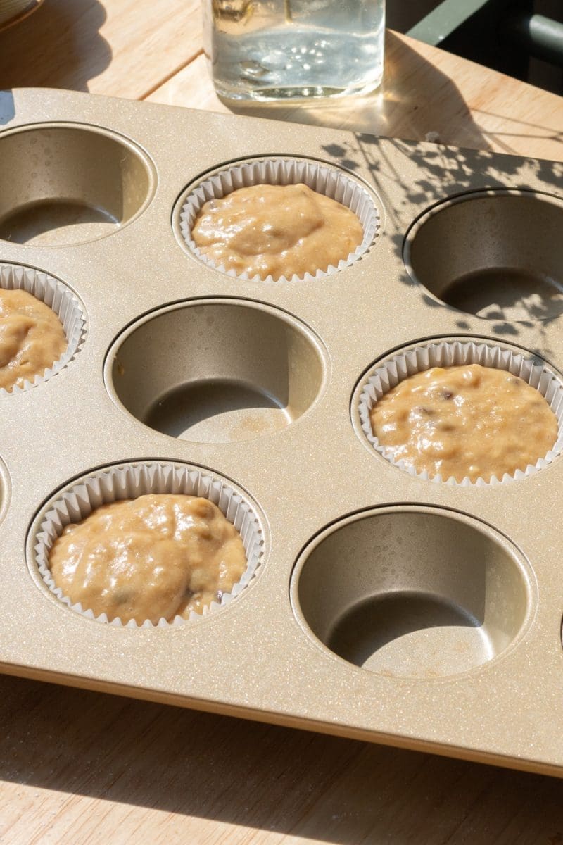 The cupcake batter split between parchment liners in a muffin tin.