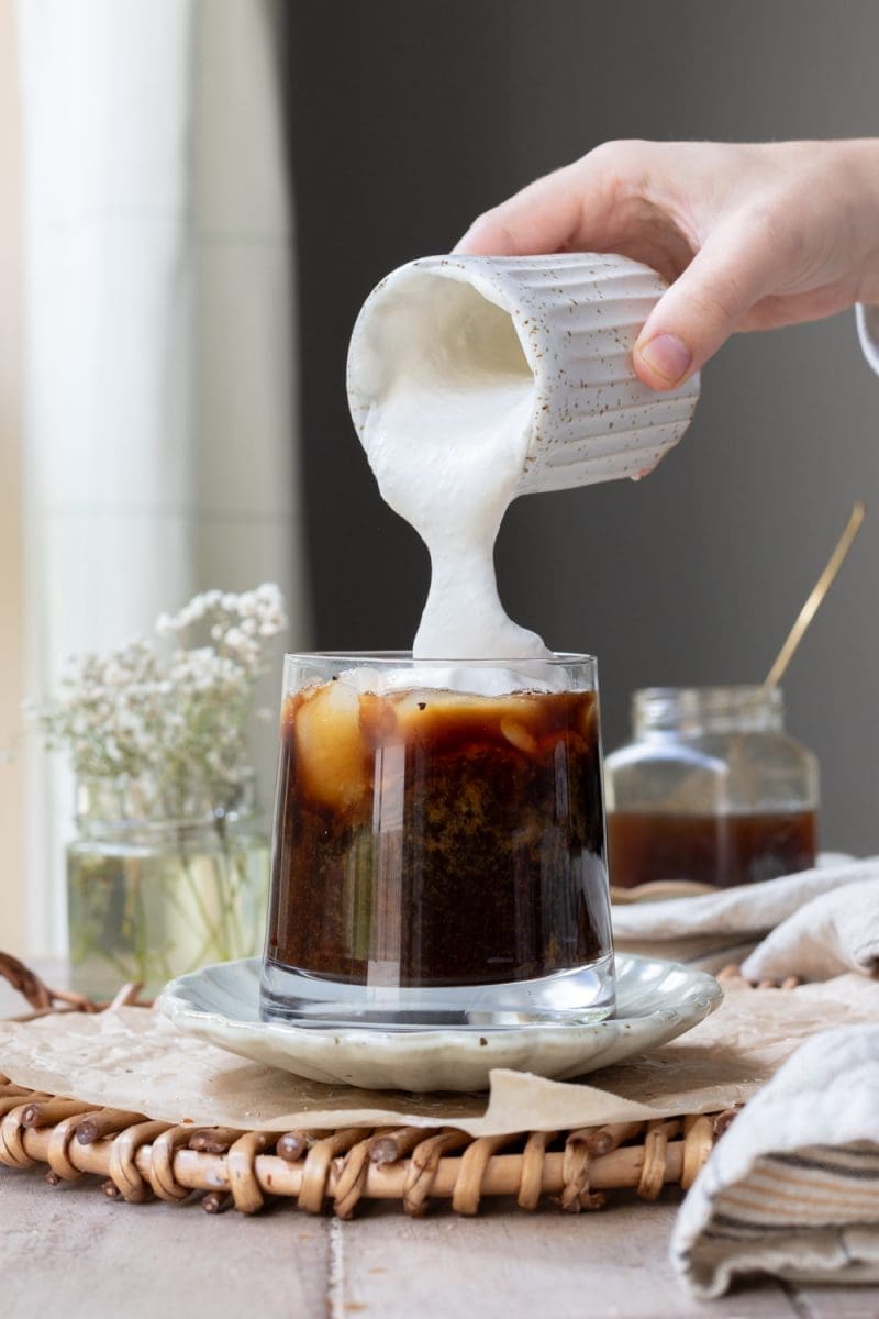 Pouring cold foam on to the coffee.