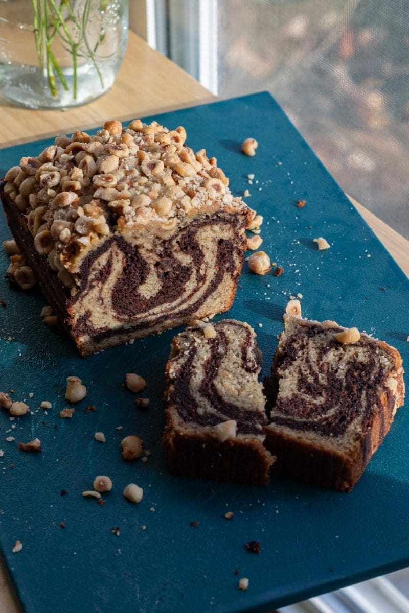 Angled view of the sliced chocolate marbled banana bread loaf with a broken slice in front of it.