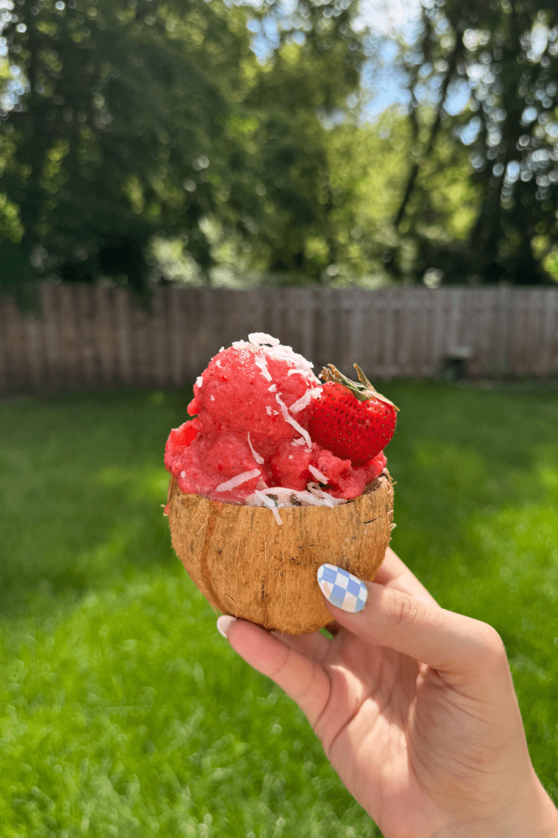 Holding up the no-churn strawberry coconut sorbet in a coconut.