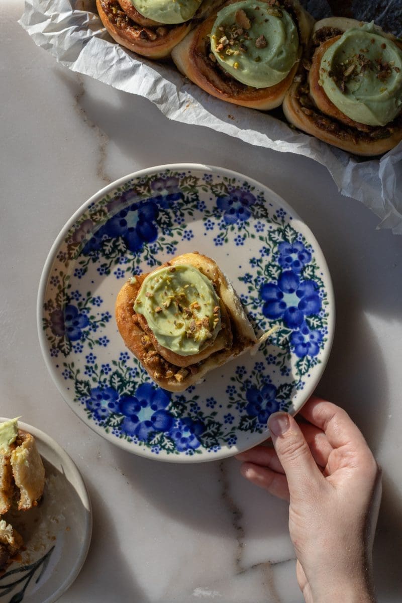 Holding a plate with one of the small batch pistachio cinnamon rolls.